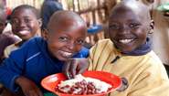 Kinder mit einem gefüllten Teller bei einer Schulspeisung im Dorf Vumbi in der Provinz Kirundo, Uganda.