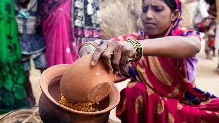 Eine Frau im Sari mit einem Ton-Gefäß in der Hand, das gefüllt ist mit Essen.