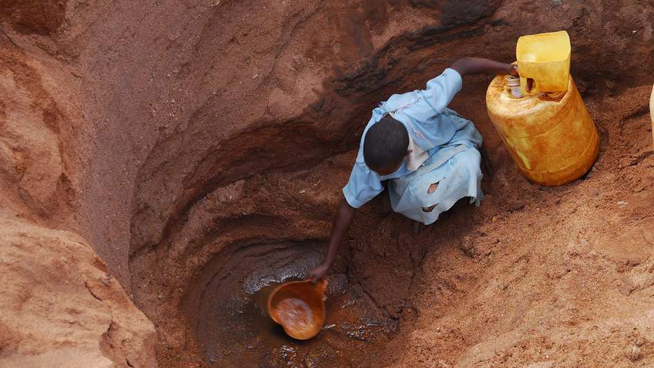 Eine Kenianerin schöpft Wasser aus einer beinahe versiegten Wasserstelle.