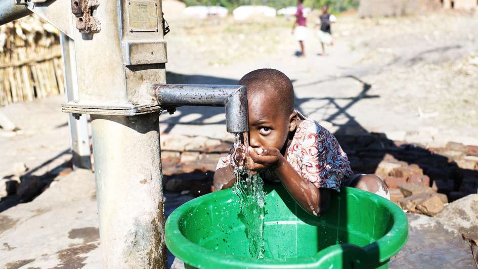 Ein Kind trinkt aus einem Brunnen.