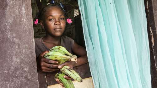 Jetzt für Kinder in Haiti spenden. Bild: Ein Kind reicht Bananen aus dem Fenster.