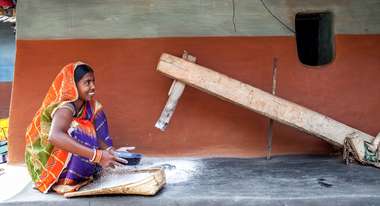 Malti Devi Gope (23) zerkleinert Reis in einem traditionellen Mahlstein in Huludbani, Jharkhand (Indien).