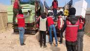 Mitarbeiter der Welthungerhilfe und SARD entladen Matratzen, Kanister und ähnliche Hilfsgüter von zwei Lkw