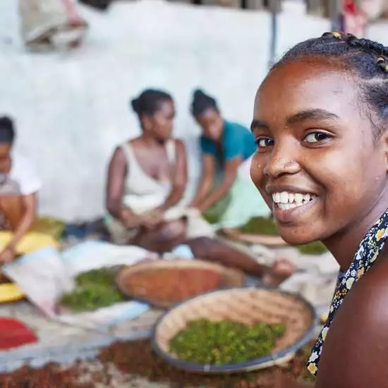 Mädchen und Frauen arbeiten in einer Pfefferfabrik, ein Mädchen im Vordergrund lächelt in die Kamera
