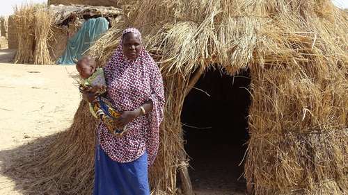 Frau mit Baby auf dem Arm vor Hütte in Nigeria