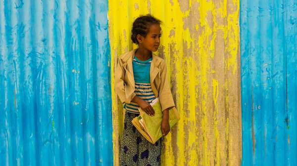 Mädchen mit Schulmappe vor blau-gelber Wand