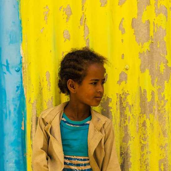 Mädchen mit Schulmappe vor blau-gelber Wand