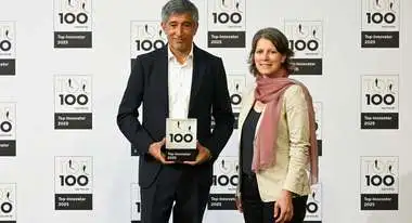 Moderator Ranga Yogeshwar und Bettina Iseli von der Welthungerhilfe posieren vor einer Fotowand, Yogeshwar hält den Top100-Preis, mit dem die Welthungerhilfe ausgezeichnet wird.
