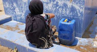 Eine Frau wartet an einer Wasserstelle darauf, dass ihr Kanister mit Trinkwasser voll wird.