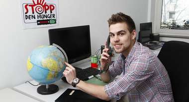 Der Auszubildende Fabio Schleicher an schaut beim Telefonieren auf einem Globus auf seinem Schreibtisch.
