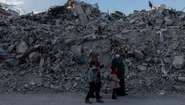 Eine Familie im türkischen Hatay steht nach de. Erdbeben 2023 vor großen Trümmerbergen.