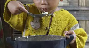 Ein kleiner Junge isst Reis aus dem Topf