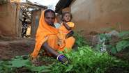 Eine indische Mutter sitzt mit ihrem kleinen Kind in ihrem Gemüsegarten.