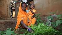 Eine indische Mutter sitzt mit ihrem kleinen Kind in ihrem Gemüsegarten.