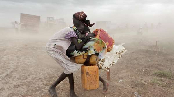 Zwei Mädchen mit Wasserkanistern versuchen sich vor einem starken Sandsturm zu schützen