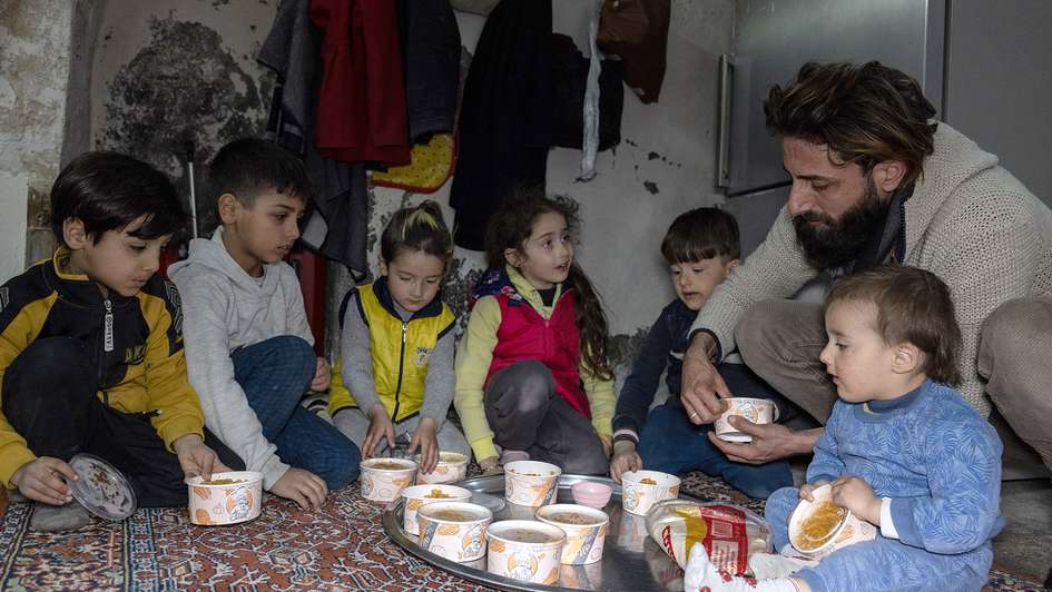 Ein Vater und sechs Kinder sitzen auf dem Boden und teilen frisches Essen unter sich auf.