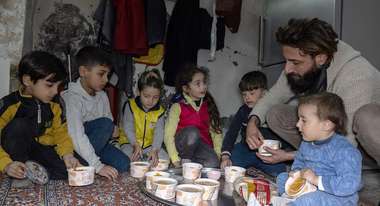 Ein Vater und sechs Kinder sitzen auf dem Boden und teilen frisches Essen unter sich auf.