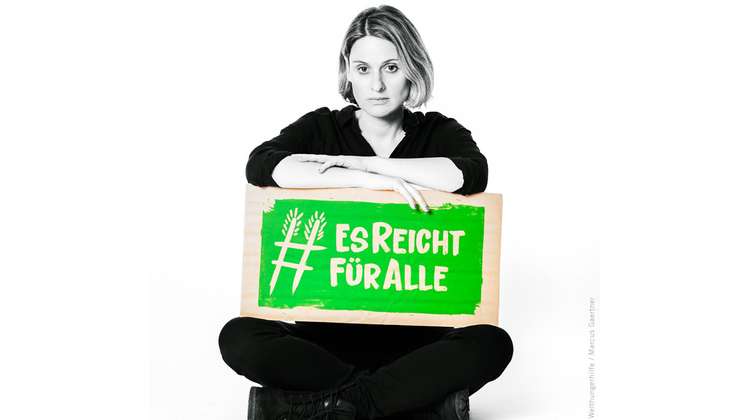 Schauspielerin und Regisserin Julia Becker hält ein Schild mit dem Welthungerhilfe-Hashtag #EsReichtFürAlle.