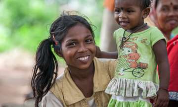 Ein Mädchen aus Pindari in Jharkand mit einem jungen Kind auf dem Schoß, Indien 2021.