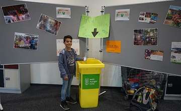 Ein kleiner Junge steht neben einer gelben Mülltonne mit Welthungerhilfe Logo 