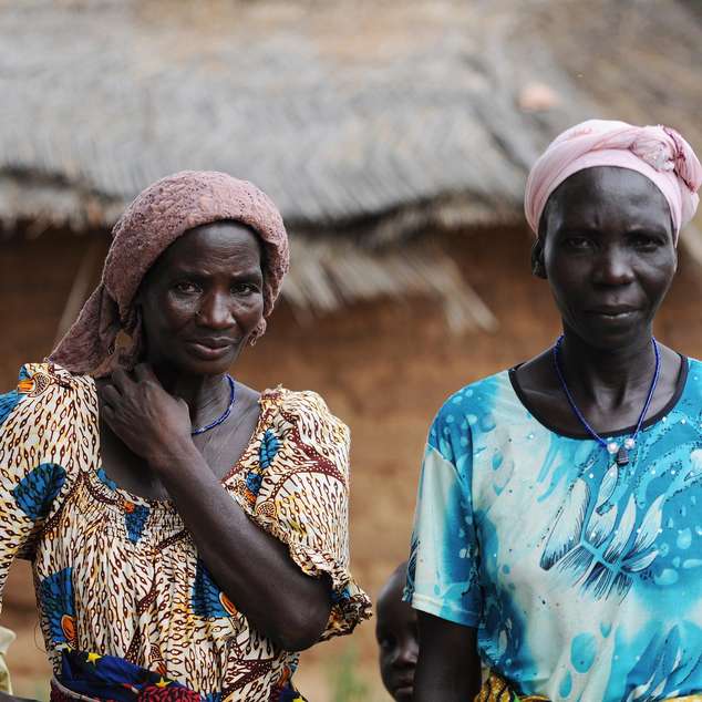 Zwei Kleinbäuerinnen in traditioneller Kleidung stehen vor einer Hütte in Burkina Faso