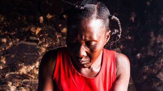 Eine Frau sitzt mit einer Schüssel in einer Hütte, Haiti 2019.