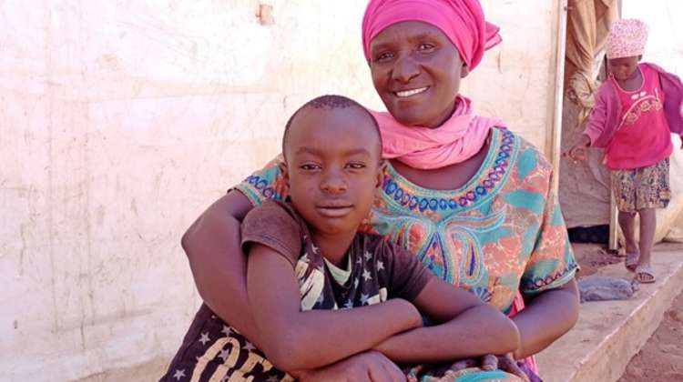 Eine Mutter sitzt auf einem Bordstein und hält ihren Sohn im Arm, Malawi 2021. 