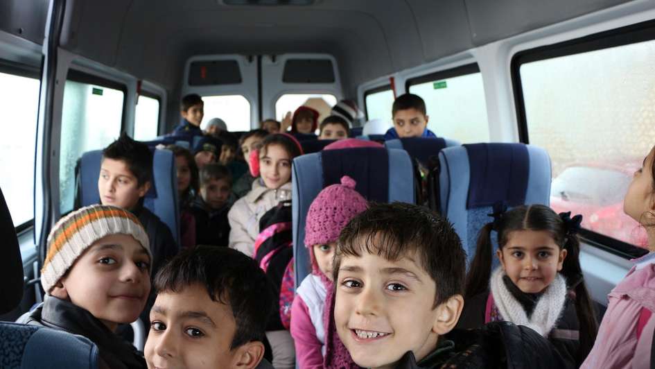 Jesidische Kinder sitzen im Schulbus und lächeln in die Kamera