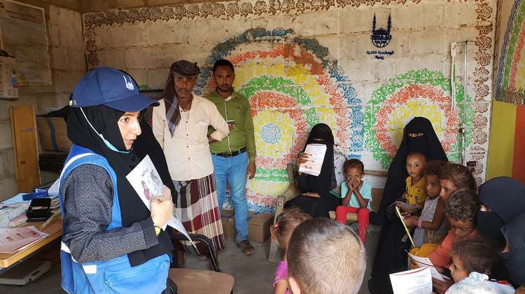 Eine Hilfsarbeiterin lehrt einer Gruppe Frauen und Kinder mithife einer Illustration Grundlagen über gesunde Ernährung.