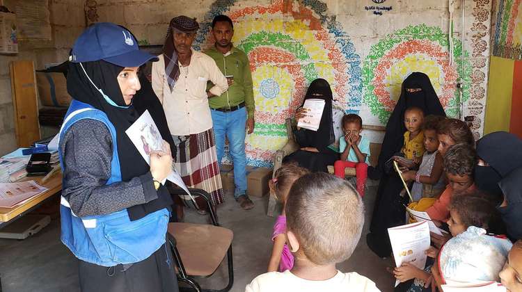 Eine Hilfsarbeiterin lehrt einer Gruppe Frauen und Kinder mithife einer Illustration Grundlagen über gesunde Ernährung.