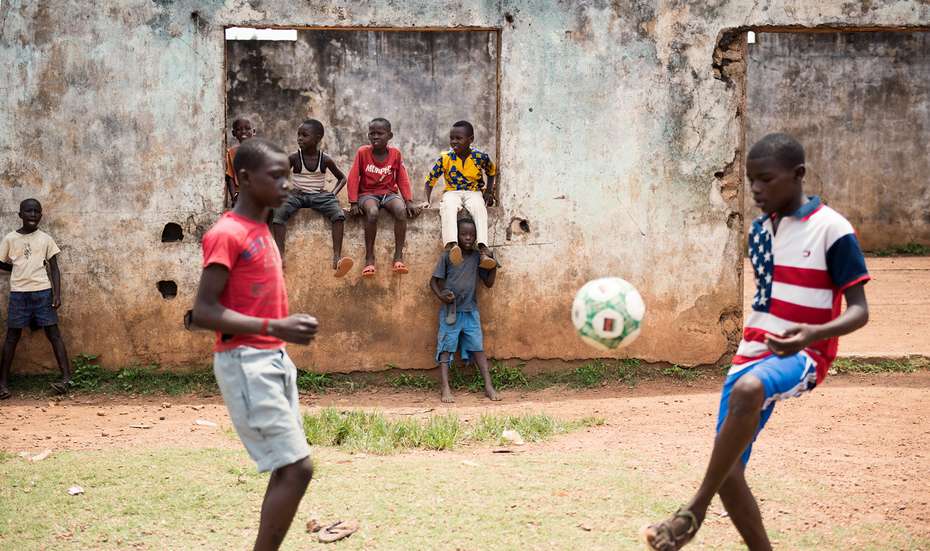 Zwei Jungen spielen Fußball. Im Hintergrund schauen weitere Kinder zu.