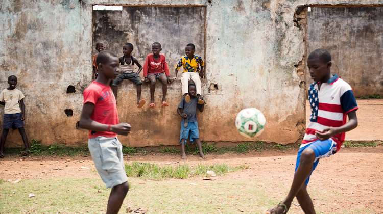 Zwei Jungen spielen Fußball. Im Hintergrund schauen weitere Kinder zu.