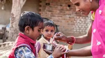 Eine Frau im Sari füttert einen kleinen Jungen.