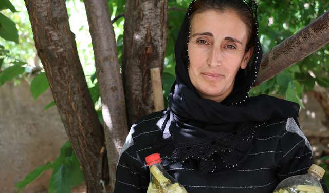 Eine Frau steht unter einem Baum, in der Hand hält sie zwei Flaschen mit Gewürzgurken, Türkei 2021.