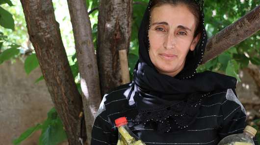 Eine Frau steht unter einem Baum, in der Hand hält sie zwei Flaschen mit Gewürzgurken, Türkei 2021.