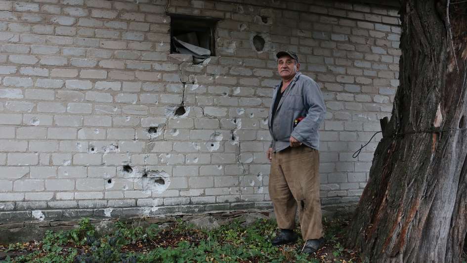 Ein Mann steht vor einem zerstörten Gebäude; symbolisch für Krieg in der Ukraine spenden, 2022.