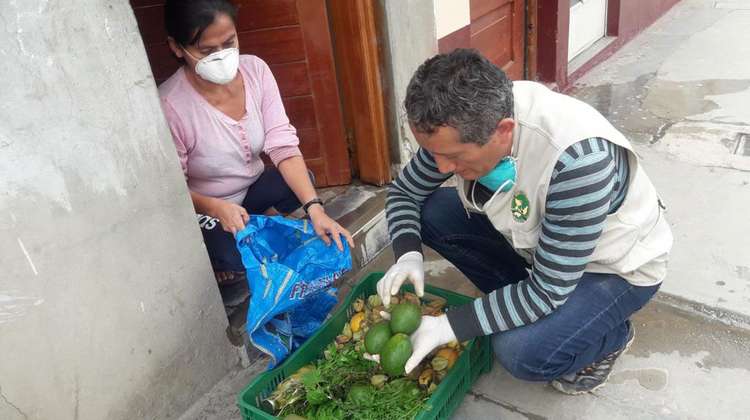 Eine Frau mit Maske kniet vor einem Korb mit Lebensmitteln, Peru 2021. 
