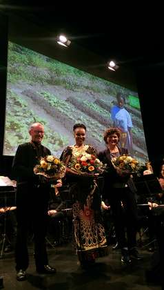 Ein Mann und zwei Frauen stehen mit Blumenstäußen auf der Bühne.