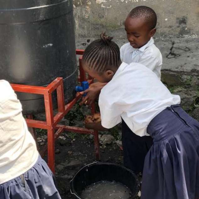Schulkinder waschen sich an einem kleinen Wassertank die Hände.