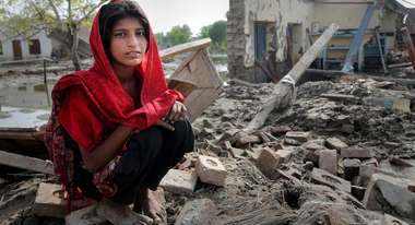 Ein Mädchen sitzt in den Trümmern ihres Hauses.