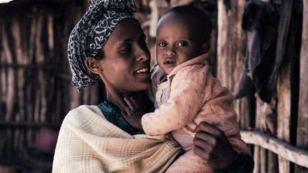 Eine Frau hält ein Baby im Arm und lächelt.