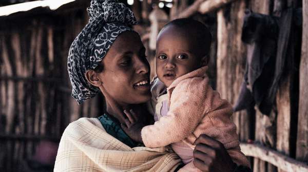 Eine Frau hält ein Baby im Arm und lächelt.