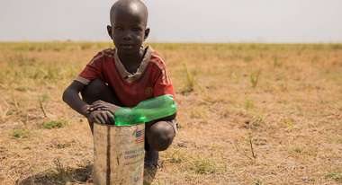 Der siebenjährige Gaodir wartet mit einer Flasche und einem Blechgefäß