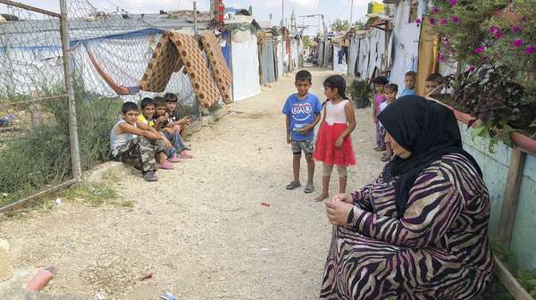 Eine Frau und mehrere Kinder sitzen und stehen auf einem Weg durch ein Camp für syrische Flüchtlinge im Libanon.