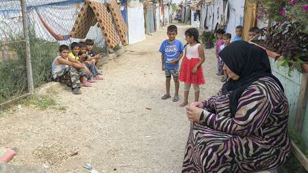 Eine Frau und mehrere Kinder sitzen und stehen auf einem Weg durch ein Camp für syrische Flüchtlinge im Libanon.
