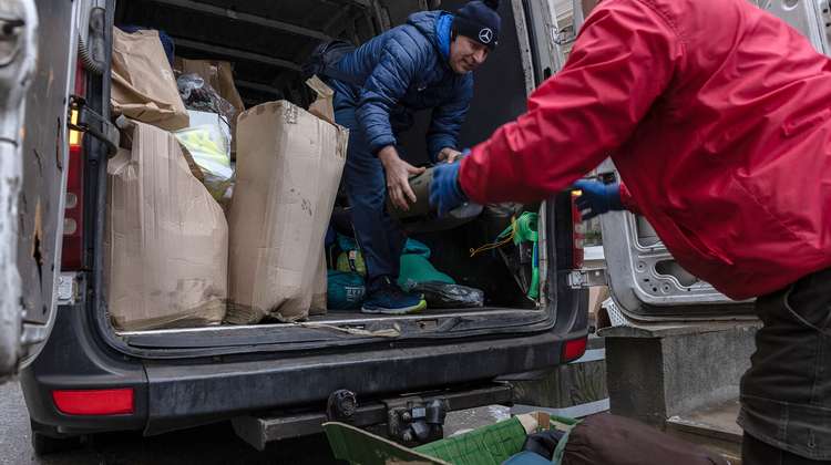 Zwei Personen in der ukrainischen Stadt Ternopil laden Hilfsgüter wie Kleidung und Decken aus einem Transporter.