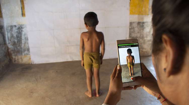 Eine Frau verwendet das Smartphone mit der Child Growth Monitor App um die Entwicklung eines Kindes zu messen, Indien 2020.