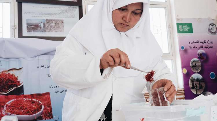 Eine Frau hält eine Pinzette mit Safran. In der anderen Hand hält sie ein Glas.