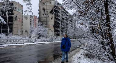 Eine Frau läuft eine Straße entlang, im Hintergrund zerstörte Wohnhäuser, es ist kalt und verschneit