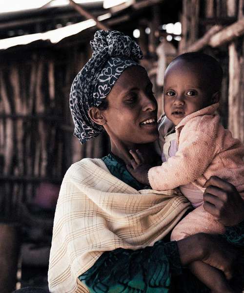 Eine Mutter mit ihrem Kind vor einer Hütte in einem Dorf in Äthiopien. Die Mutter lächelt das Kind an.